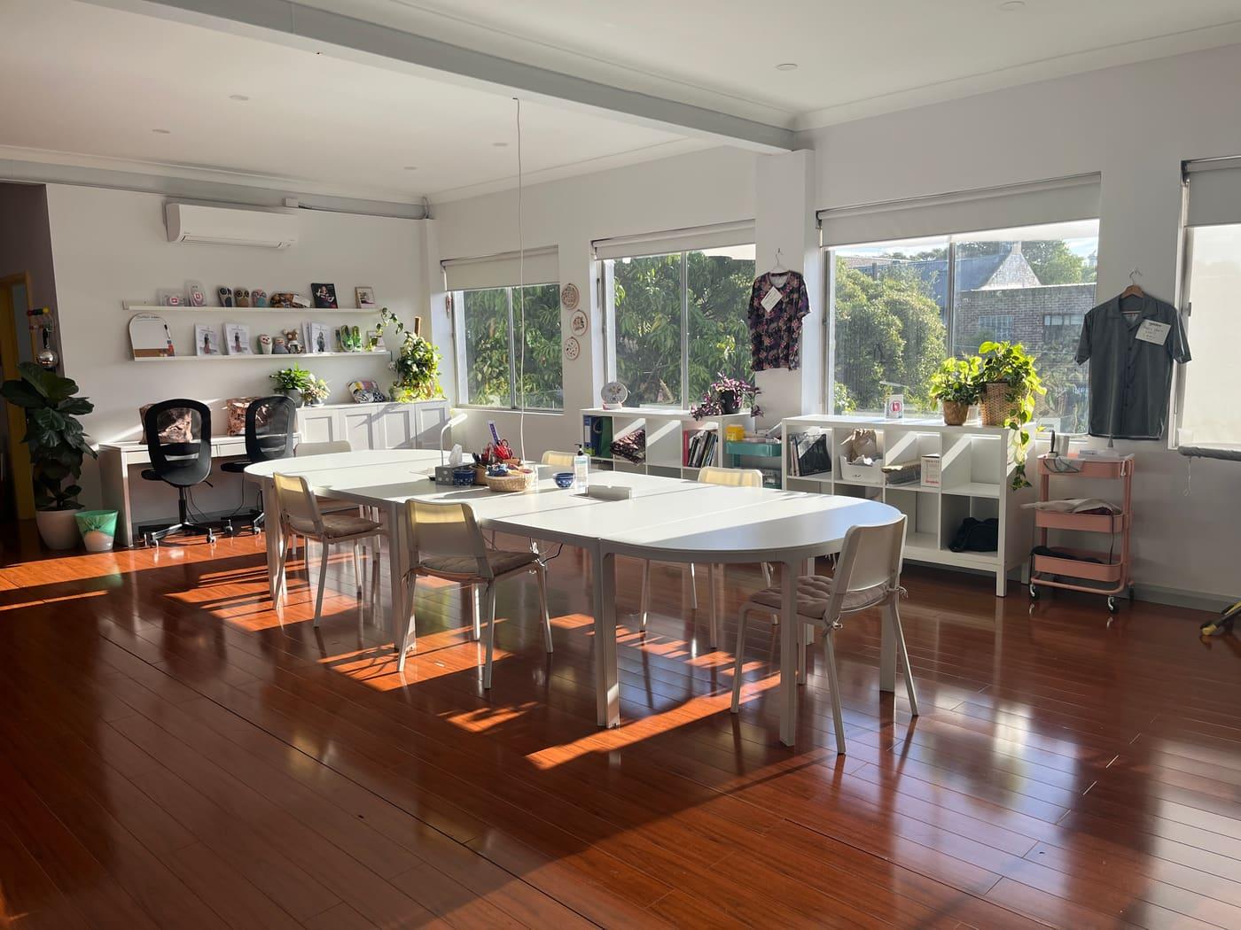 The Main Studio in afternoon sun, the big table set up with chairs and plants along the windows.