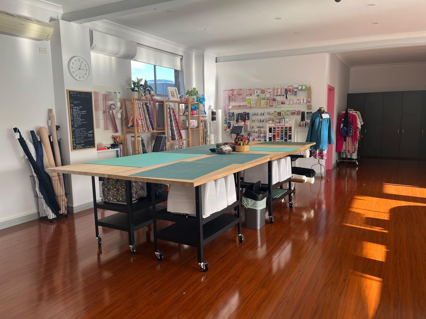 The Main Studio: a long cutting table with a green mat, the chalkboard of term dates on the left and the haberdashery wall on the right.