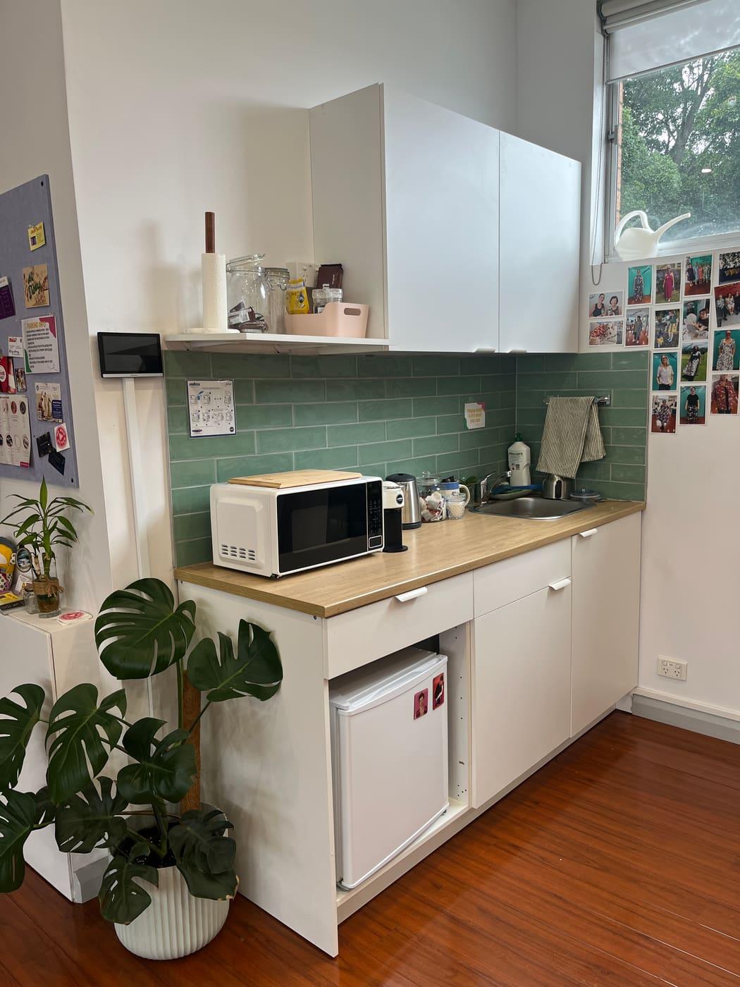 The studio kitchen: green tiled splashback, microwave, kettle, sink and fridge.